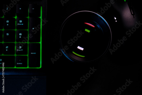 Obiettivo fotocamera visto dall'alto con riflesso appoggiato su scrivania con tastiera e mouse da gaming
