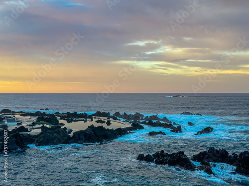 Panoramic sunset view of volcanic rock formation Ilheu Mole in coastal town Porto Moniz, Madeira island, Portugal, Europe. Rugged coastline of majestic Atlantic Ocean. Waves smashing against shoreline photo