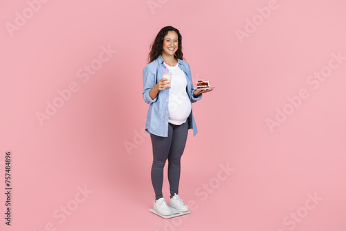 Happy young expecting lady holding glass of milk and cake © Prostock-studio