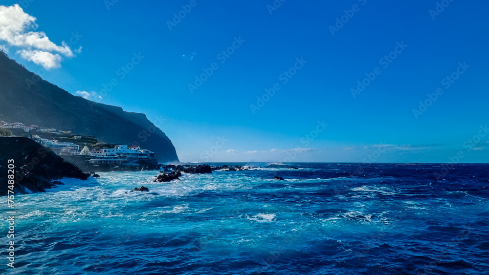 Strong waves smashing against jagged volcanic rocks on coastline of coastal town Porto Moniz, Madeira island, Portugal, Europe. Panoramic view of natural swimming pools of majestic Atlantic Ocean