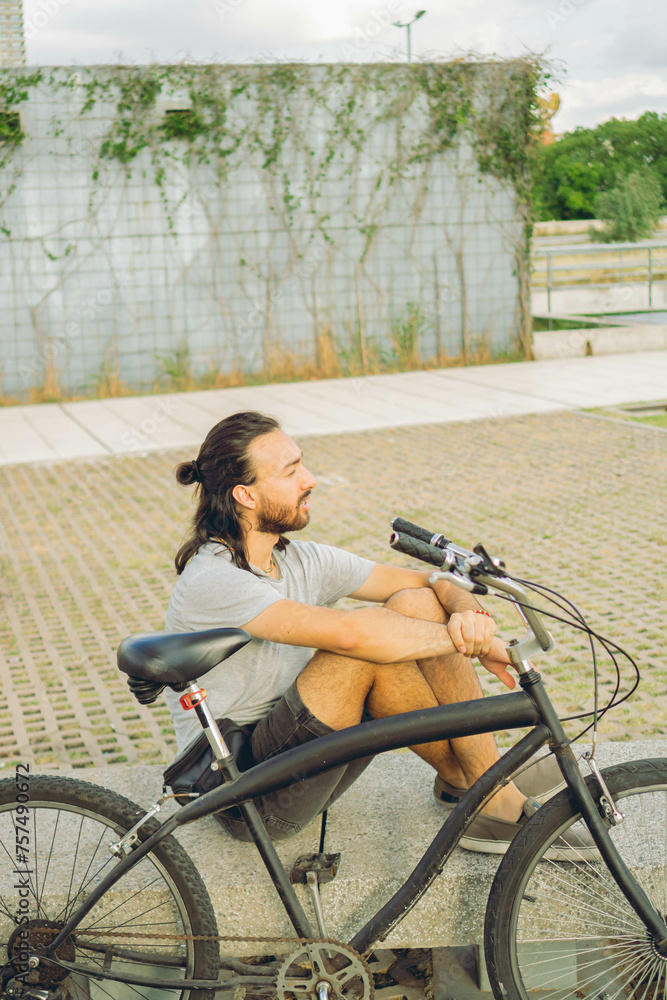 Obraz premium young latin man resting pensively on a bench next to his bicycle
