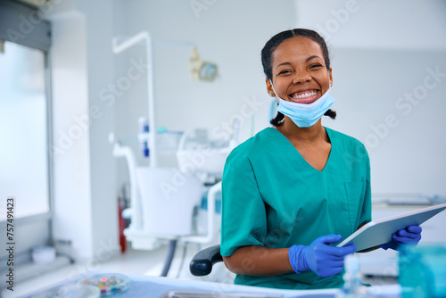 Happy black dentist using touchpad while working at her office and looking at camera.