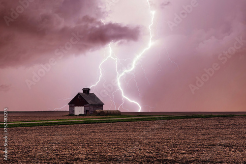 One rural barn, house in the middle in field on stormy sky with lightning strike background.