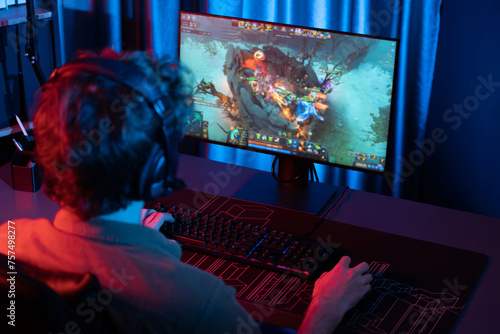 Host channel of young gaming streamer playing fighting Moba at battle arena game with multiplays team, wearing headphone on pc monitor with back side image at neon digital light modern room. Gusher. photo