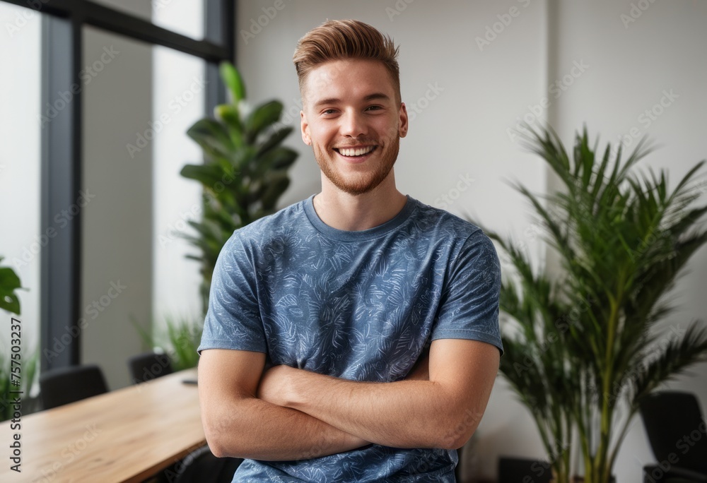 Fototapeta premium A happy man stands with his arms crossed in a modern office. His casual blue shirt and beaming smile project confidence and approachability.