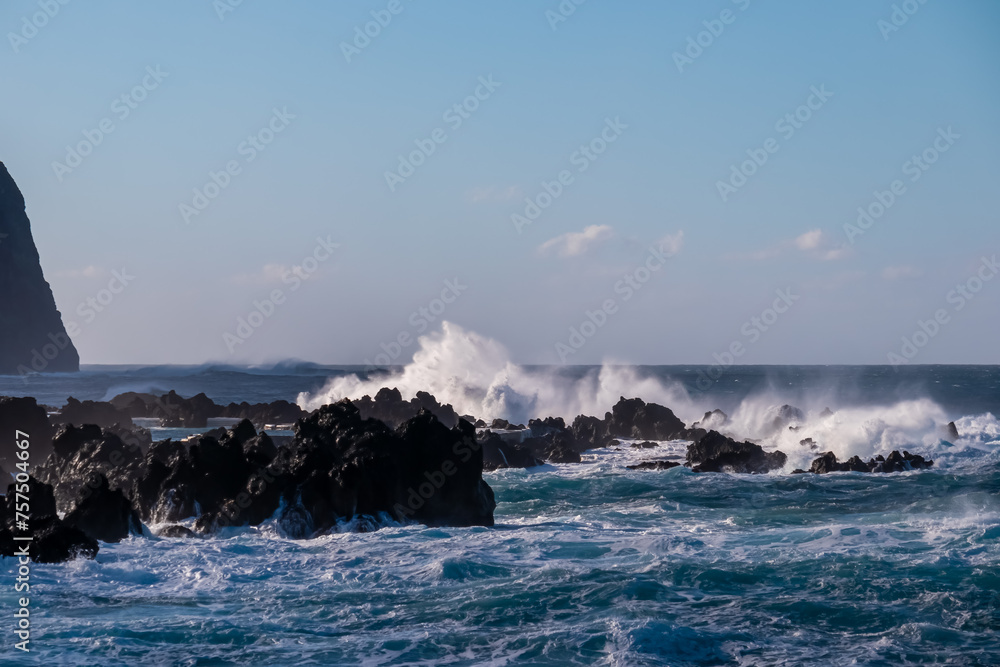 Strong waves smashing against jagged volcanic rocks on pristine coastline of coastal town Porto Moniz, Madeira island, Portugal, Europe. Powerful natural forces of majestic Atlantic Ocean. Seascape