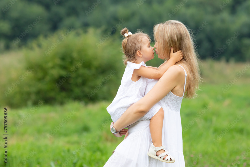 Beautiful young mom carrying and hugging her cute little daughter in the park. side view. Mom and daughter have fun together outdoor on green meadow. Happy Motherhood and family time concept Beautiful young mom carrying and hugging her cute little daughter in the park. side view. Mom and daughter have fun together outdoor on green meadow. Happy Motherhood and family time concept