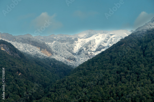 Photograph of snow on a mountain that is in a green valley in Fiordland National Park on the South Island of New Zealand