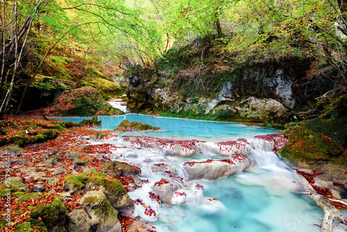The Urederra River flows through Urbasa Forest, creating a magical scene with its turquoise waters and autumn leaf-strewn banks photo