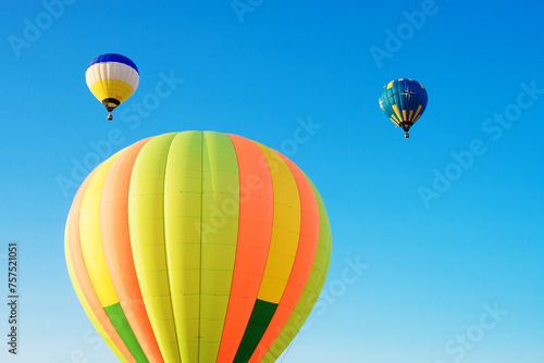 Multi-colored hot-air balloons soar in the morning blue sky.