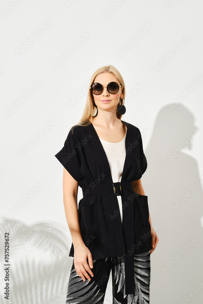 Woman wearing black outer garment paired with a white top and patterned pants Woman wearing black outer garment paired with a white top and patterned pants