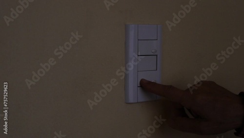 El hombre prende la luz de su hogar con el interruptor de luz presionando con el dedo en el pulsador,  permitiendo que el circuito eléctirco se ponga en funcionamiento photo