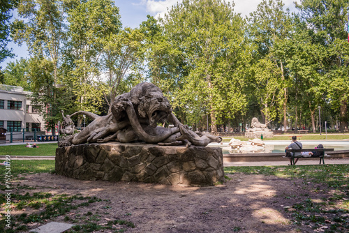 Sculpture of a lion fighting a snake in Montagnola park and people relaxing by the lake, Bologna ITALY
