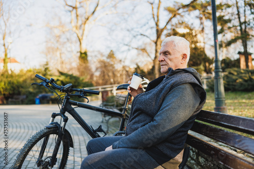 Man Sitting Next to Bike Drinking From Coffee Cup on a Park Bench