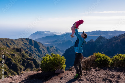 Happy father lifting up toddler with scenic view of misty hills and canyons of rugged terrain on Madeira island, Portugal, Europe. Idyllic hiking trail to mountain peak Pico Ruivo. Aerial vista