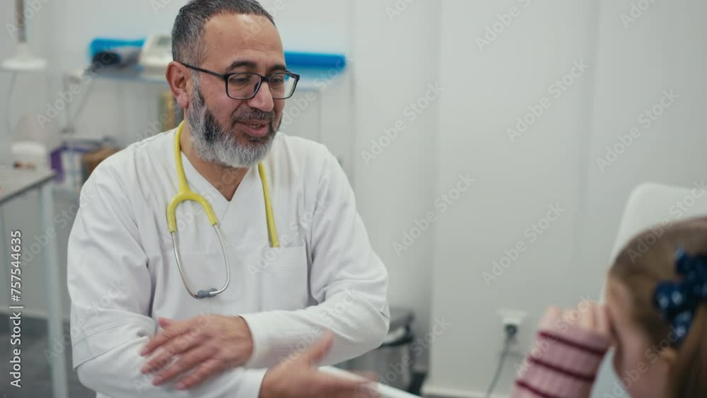 At an appointment with a family doctor, a little girl hugs a male doctor as a sign of gratitude for taking care of her health, while in the office of a modern clinic At an appointment with a family doctor, a little girl hugs a male doctor as a sign of gratitude for taking care of her health, while in the office of a modern clinic