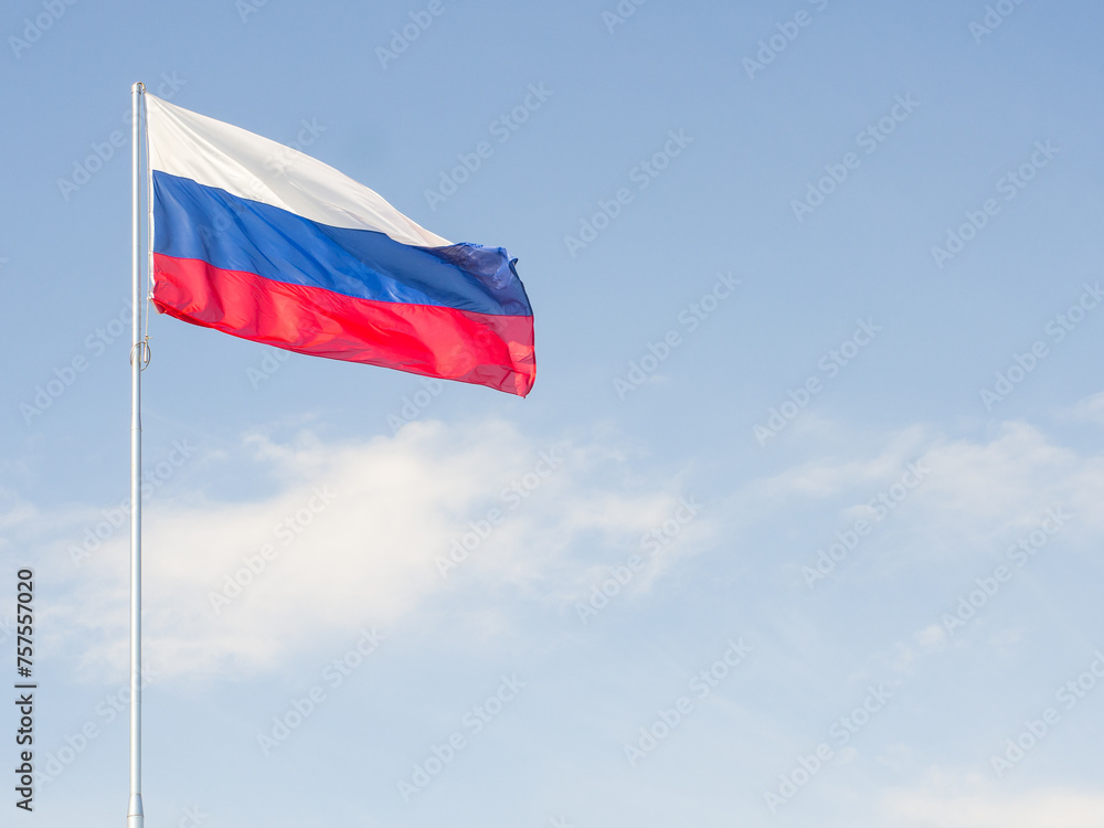 Flag of Russia waving in the wind against a blue sky with clouds