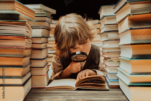 Little researcher boy reads book with magnifying glass in library. Cute clever preschooler playing, studying knowledge with instrument