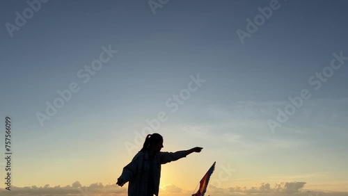 A person is happily flying a kite in the sky as the sun sets, enjoying leisure time amidst the beautiful landscape with a gesture of freedom and recreation photo