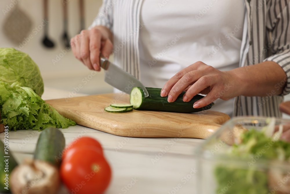 Woman cutting cucumber at white marble table, closeup Woman cutting cucumber at white marble table, closeup