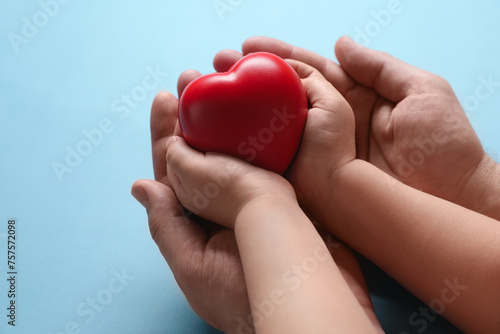 Father and his child holding red decorative heart on light blue background, closeup