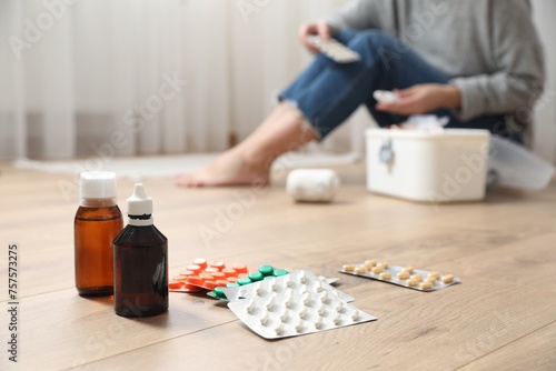 Woman with first aid kit sitting on floor indoors, focus on medicaments