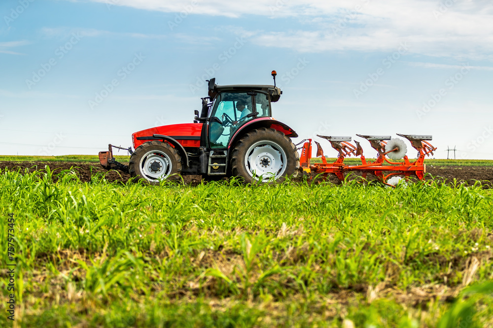 Tractor with plowing equipment preparing the soil in a green field under a clear sky Tractor with plowing equipment preparing the soil in a green field under a clear sky