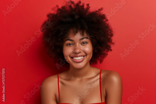 Positive smiling dark-skinned girl with curly dark brown hair looking at camera on bright red background