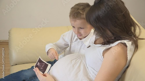 Mother showing to her son her pregnant belly and the ultrasound picture photo