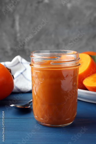 Delicious persimmon jam in glass jar and fresh fruits on blue wooden table