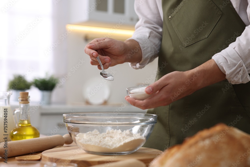 Making bread. Man putting salt into bowl with flour at wooden table in kitchen, closeup Making bread. Man putting salt into bowl with flour at wooden table in kitchen, closeup