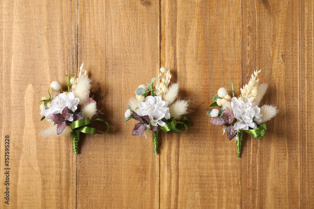 Stylish boutonnieres on wooden table, flat lay Stylish boutonnieres on wooden table, flat lay