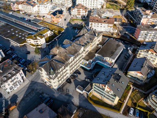 Aerial view of Engelberg, Switzerland, showcasing a large hotel with a white facade, colorful leisure buildings, diverse architecture, and a train station, under clear skies. photo