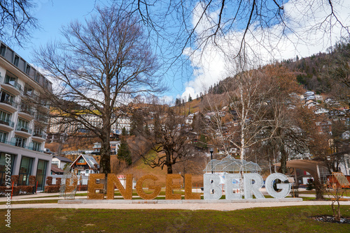 Scenic view of Engelberg resort with a reflective ENGELBERG sign on a lawn, a luxury hotel with modern architecture, and treecovered mountains in the background. photo