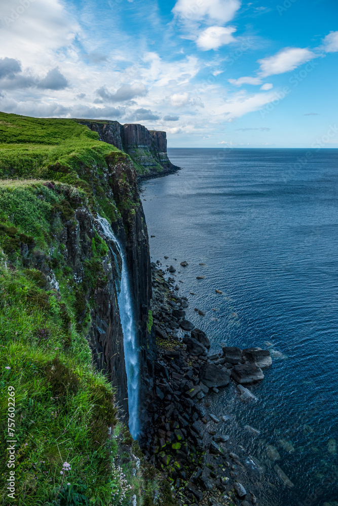 Stunning coastline with high cliffs and waterfall cascading down to rocky shore