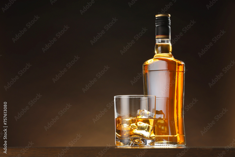 Obraz premium Whiskey with ice cubes in glass and bottle on table, space for text