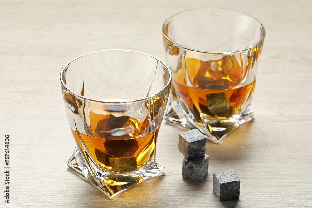 Whiskey stones and drink in glasses on light wooden table, closeup Whiskey stones and drink in glasses on light wooden table, closeup