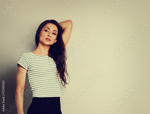 Beautiful young relaxing woman in casual clothing thinking and looking behind on blue studio background on empty copy space. Closeup