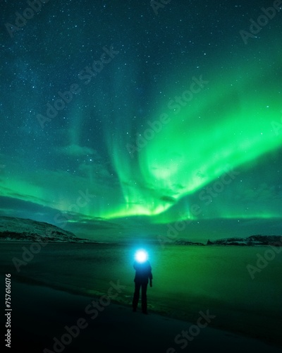 Northern lights over a Norwegian fjord with person and headlamp, Tromso, Norway, Europe photo