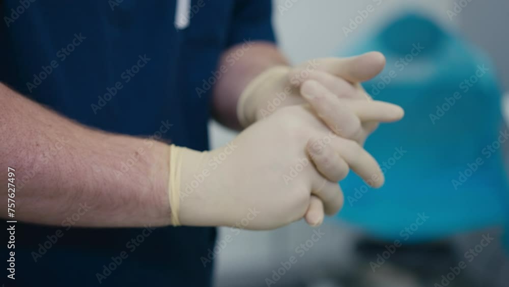 Close-up. A man in blue medical clothing puts thin medical gloves on his hands Close-up. A man in blue medical clothing puts thin medical gloves on his hands
