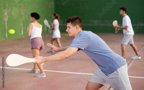 Young male pelota player hitting ball with wooden paleta during training game on outdoor Basque pelota fronton. photo
