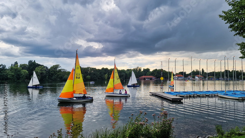 Sailboats glide on cloudy lake, against natural landscape backdrop Maschsee Hanover Germany