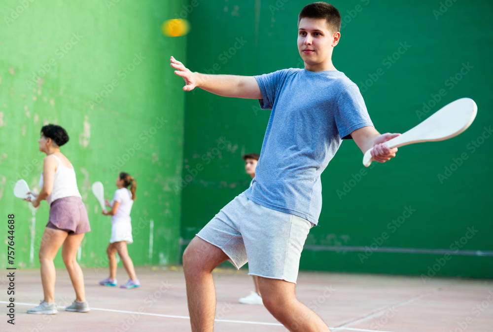 Young man playing Basque pelota on outdoor pelota court during training. Teenager playing pelota speciality with wooden paleta.
