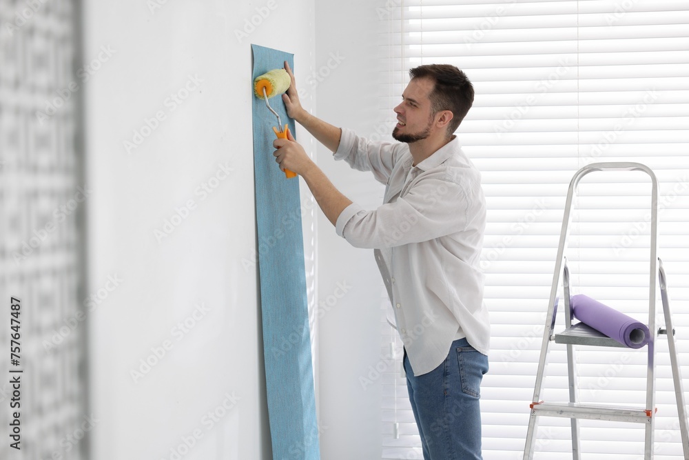 Man hanging light blue wallpaper in room