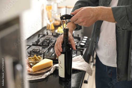 Man opening wine bottle with corkscrew at black countertop indoors  closeup