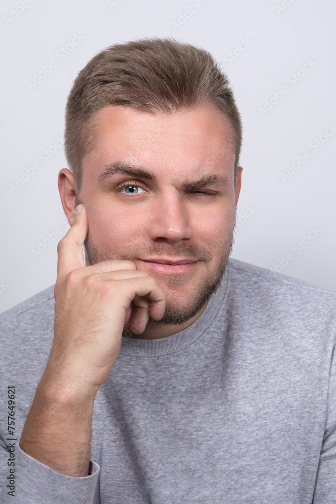 A young blond man with a goatee smiles, squinting one eye directly at the camera