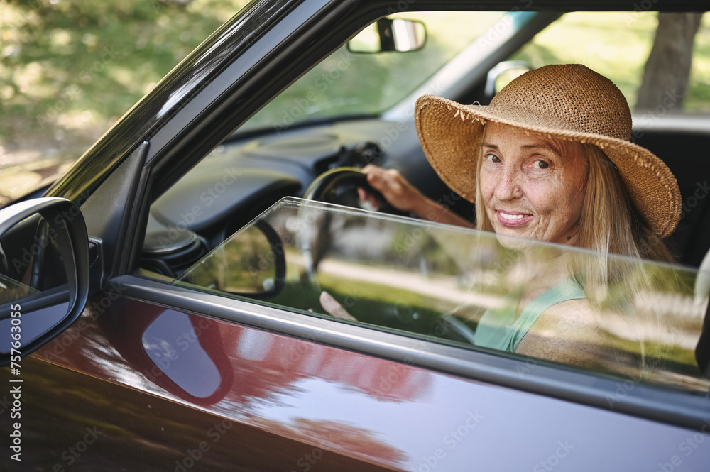 Straw Driver Happy senior woman driver in straw hat driving sitting in new car ...