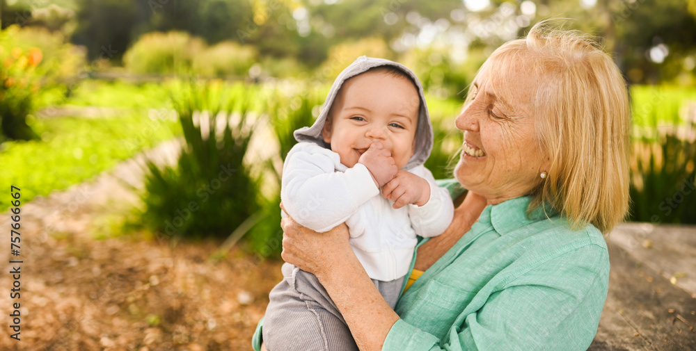 Fototapeta premium Beautiful happy smiling senior elderly woman holding on hands cute little baby boy. Grandmother and grandson having fun time together at tropical summer day in park. Multigenerational family concept