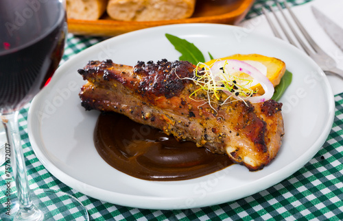 Roasted spicy pork ribs served on white plate in chocolate sauce with baked potatoes and greens