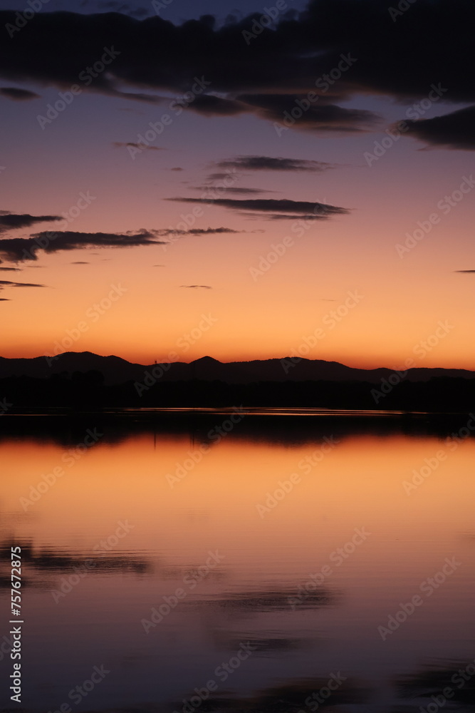 Colourful sunset over a flat lake with mountains in the background and clouds reflecting in water